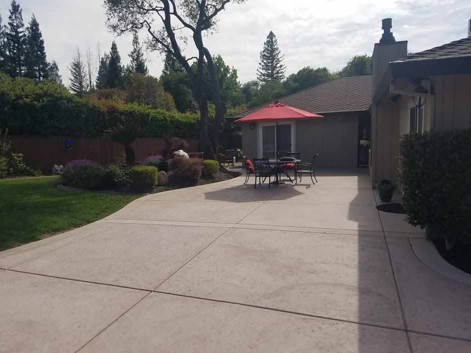 Backyard concrete patio with outdoor dining area and professional landscaping